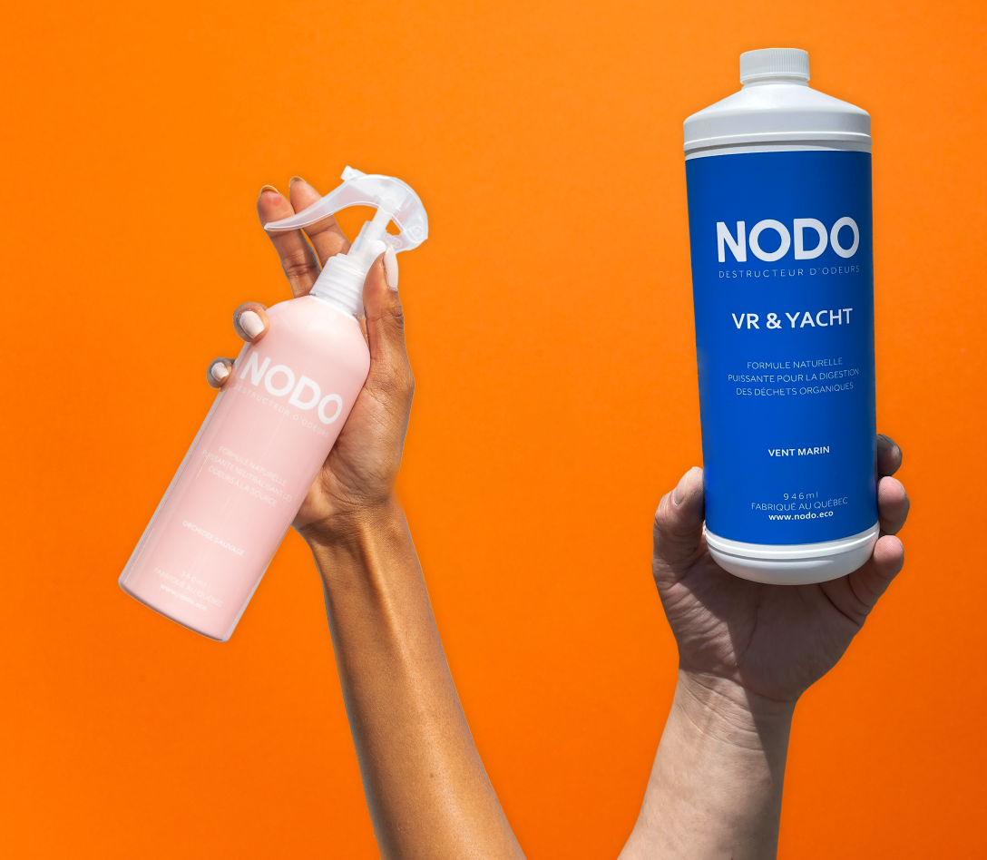 Des destructeurs d'odeurs naturels NODO tenues par des mains. Un neutralisant d'doeur en vaporisateur à l'arôme d'orchidée sauvage et un éliminateur d'odeurs pour les toilettes septiques à l'arôme de vent marin.