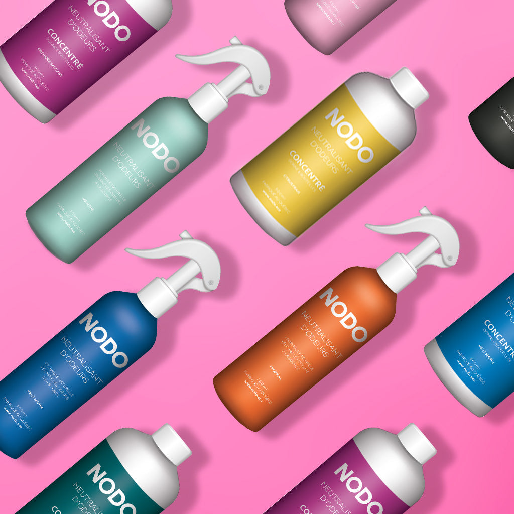 Photo flat lay des produits NODO neutralisants d’odeurs – bouteilles vaporisateurs et concentrés – disposés sur fond rose éclatant. Étiquettes colorées : Citrus Frais, Menthe, Orchidée Sauvage, Tropical, Gomme Balloune, Vent Marin.