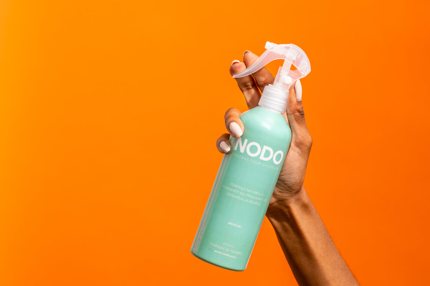 Vaporisateur éliminateur d'odeurs NODO à l'arôme de menthe tenu dans une main sur fond orange